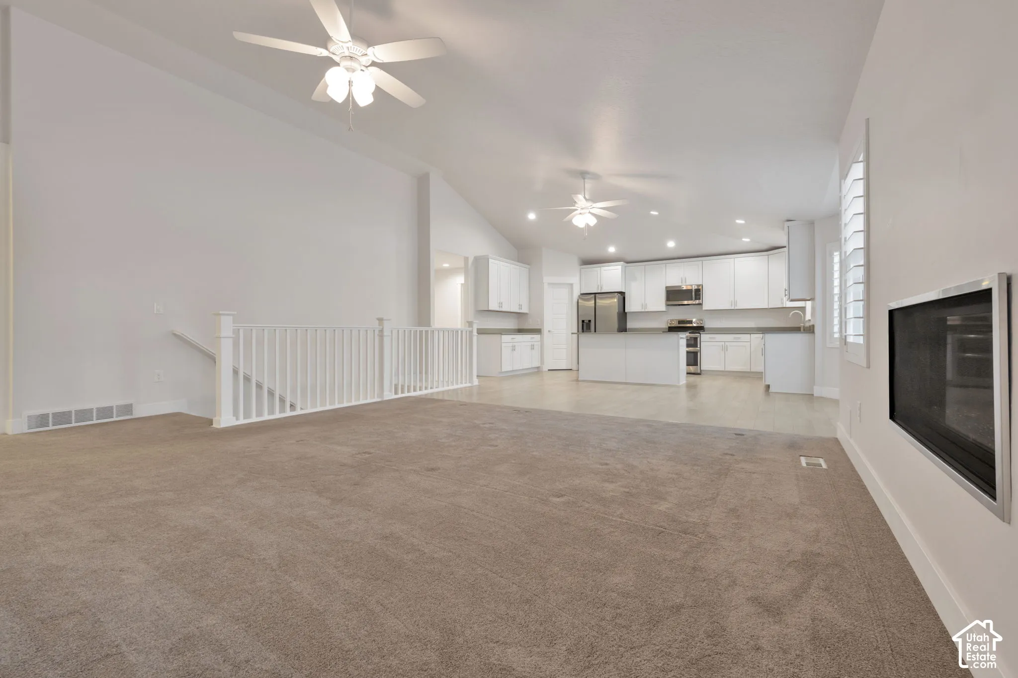Open-concept floor plan featuring vaulted ceilings, recessed lighting, dual ceiling fans, a wall-mounted fireplace, and white cabinetry