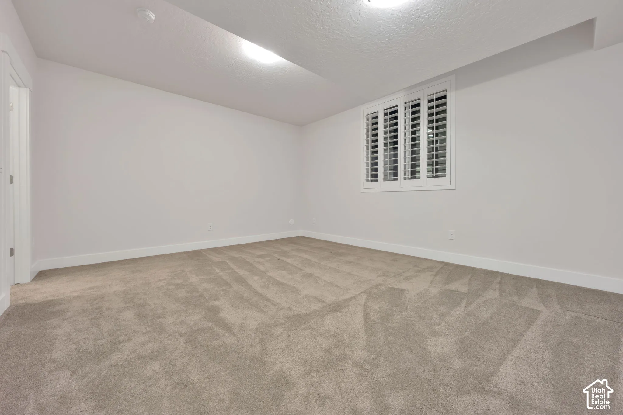 Room featuring neutral wall-to-wall carpeting, white walls, and a window fitted with white plantation shutters