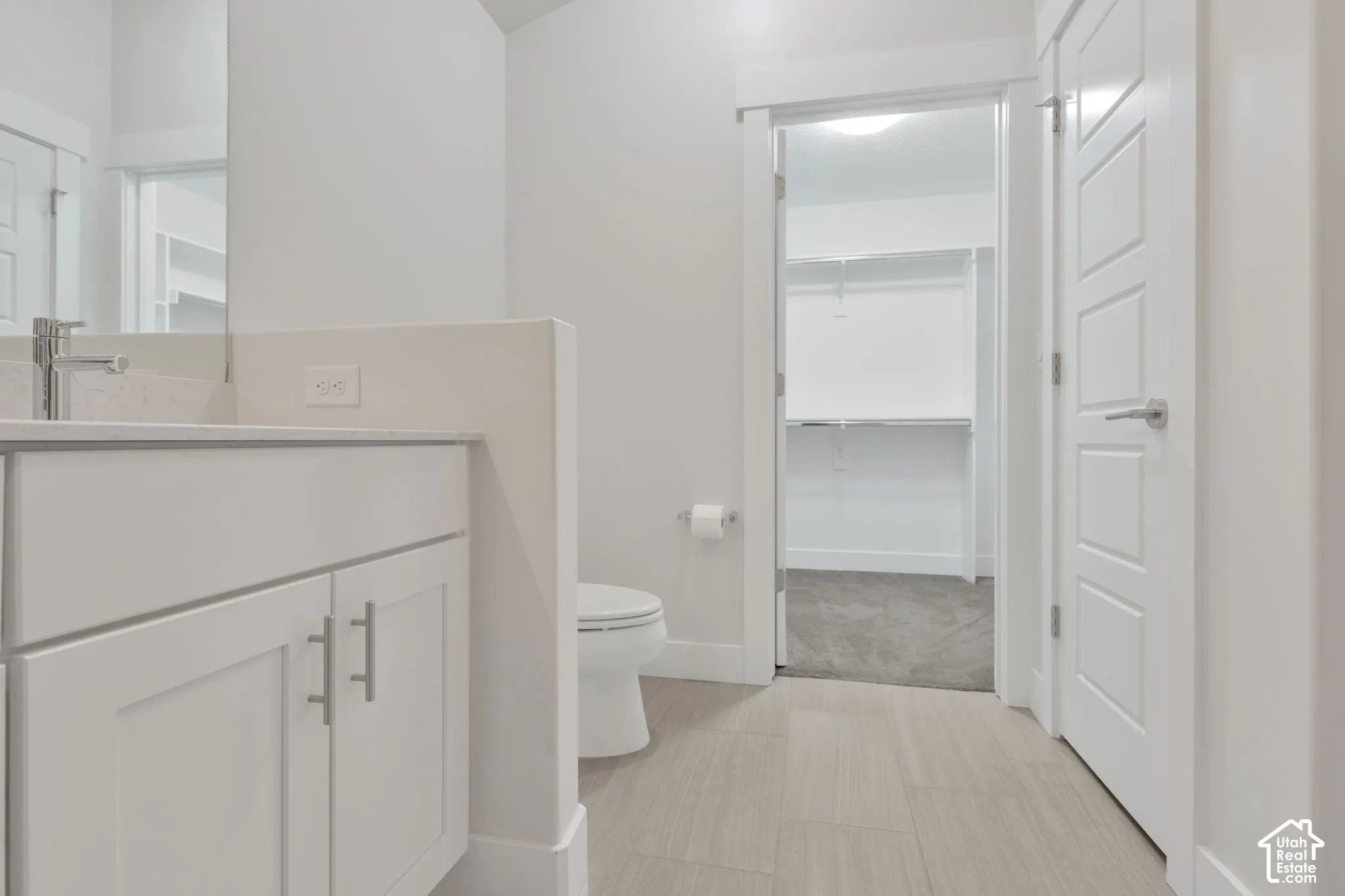 Bathroom featuring a vanity with shaker-style cabinetry, and rectangular undermount sink, complemented by light-toned tile flooring and a walk-in closet with built-in shelving