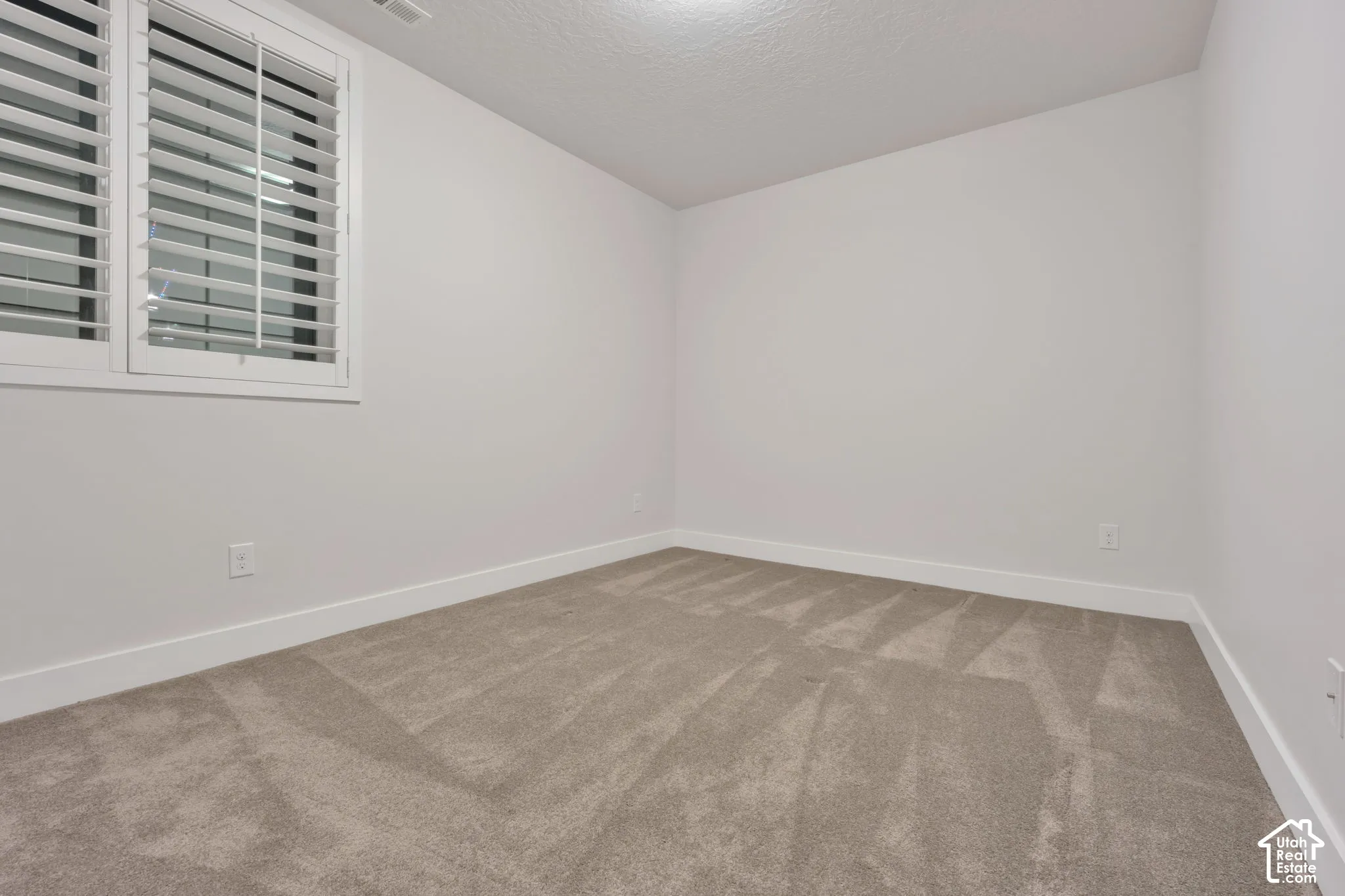 Neutral-toned carpeted flooring, walls finished in a crisp neutral paint, and window shutters
