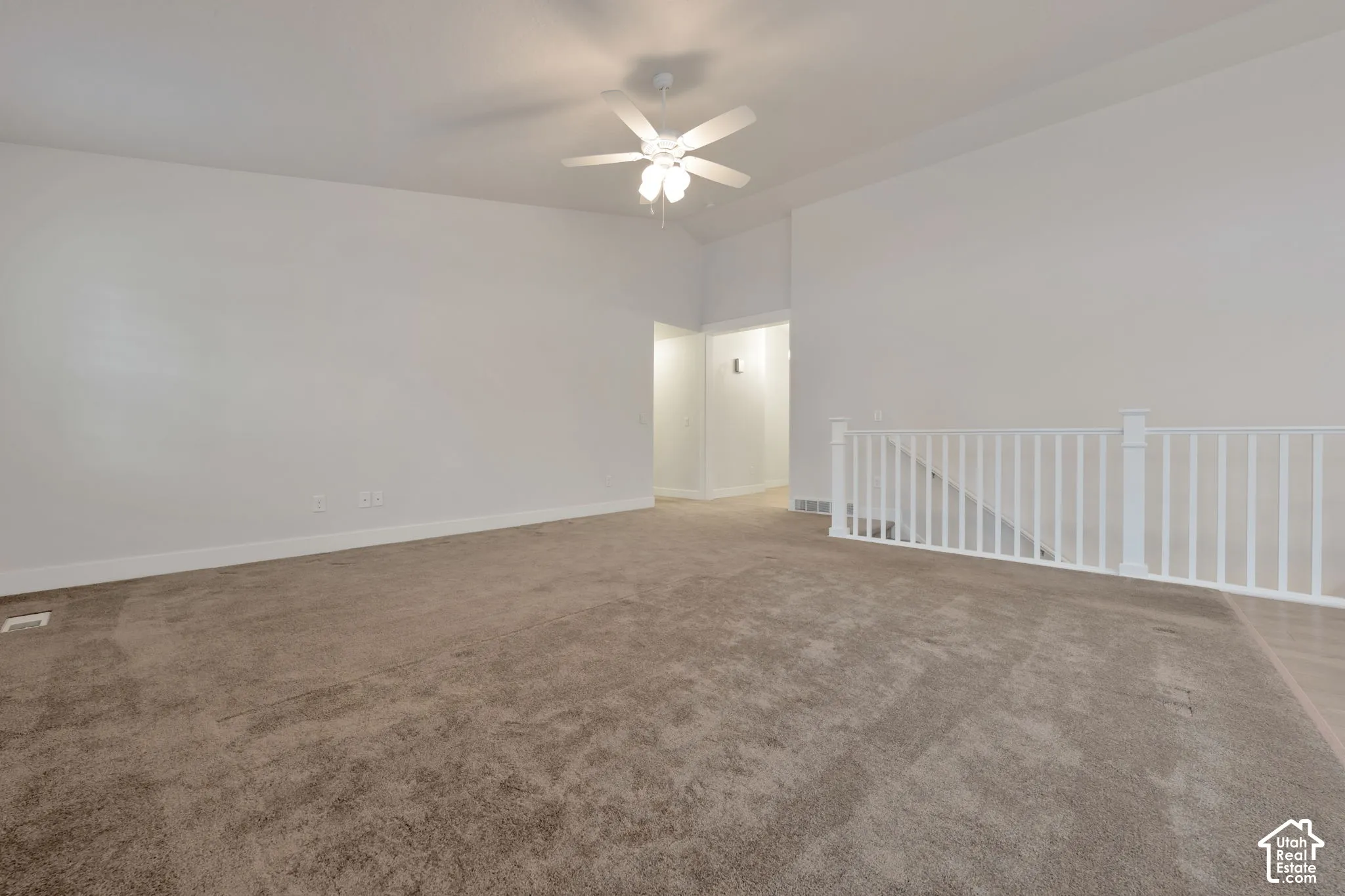 Vaulted ceiling, wall-to-wall carpeting, ceiling fan with integrated lighting, and white wooden balustrade railing