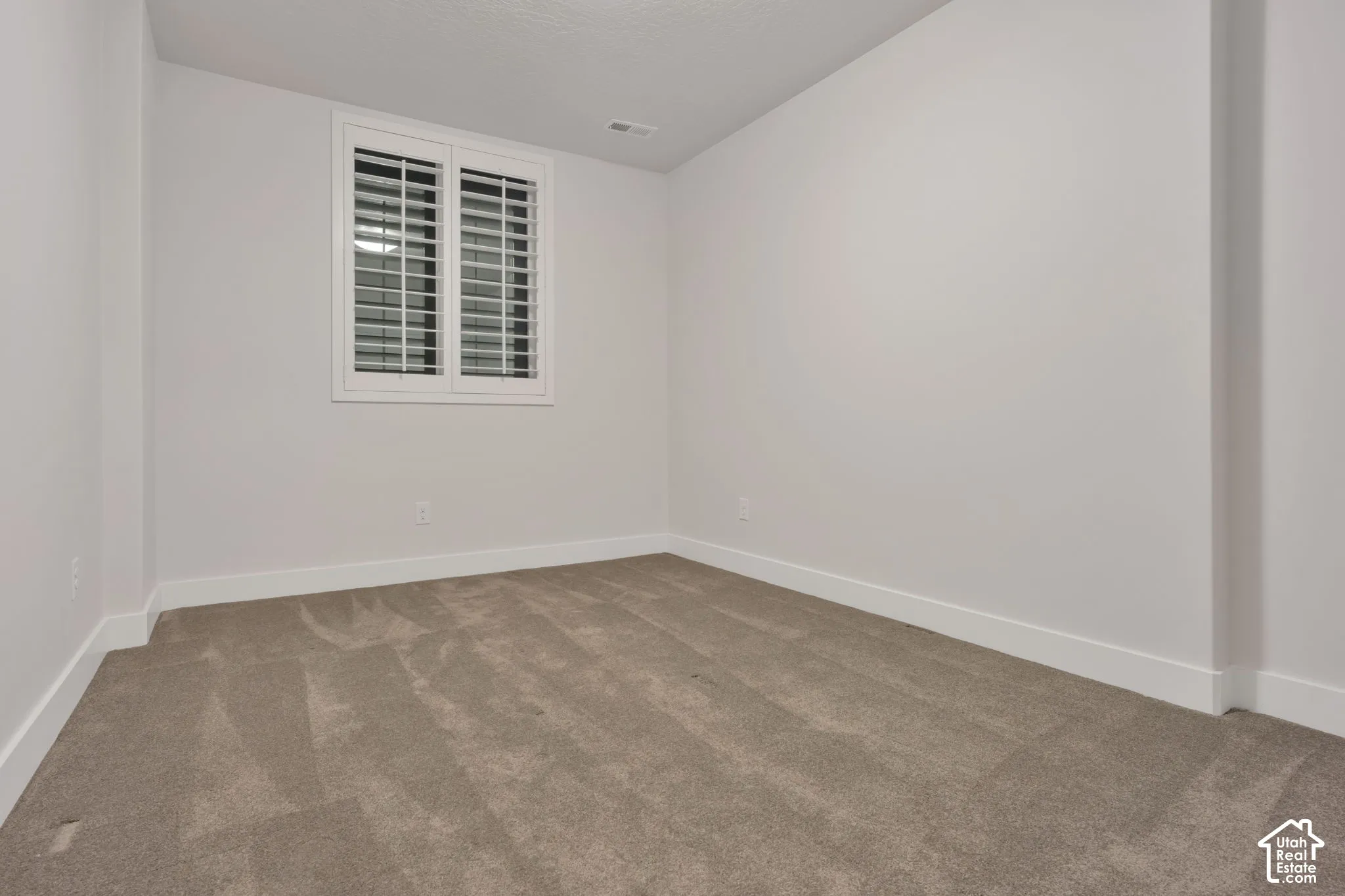 Neutral-toned room featuring neutral carpeting, crisp white wall finishes, and custom white interior window shutters