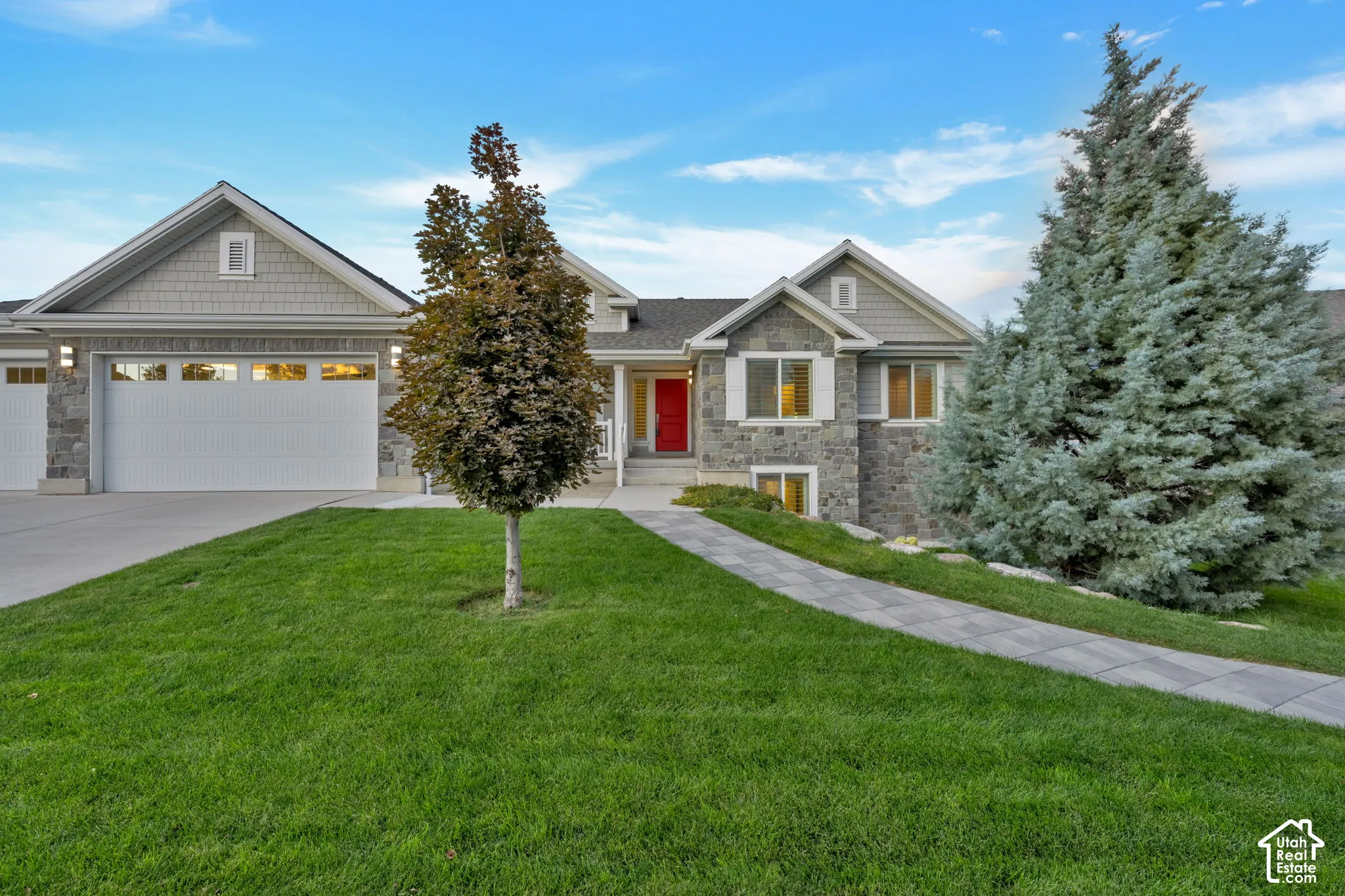 Stone veneer and shake siding exterior featuring a three-car garage, concrete driveway, paved walkway, and a vibrant red entry door