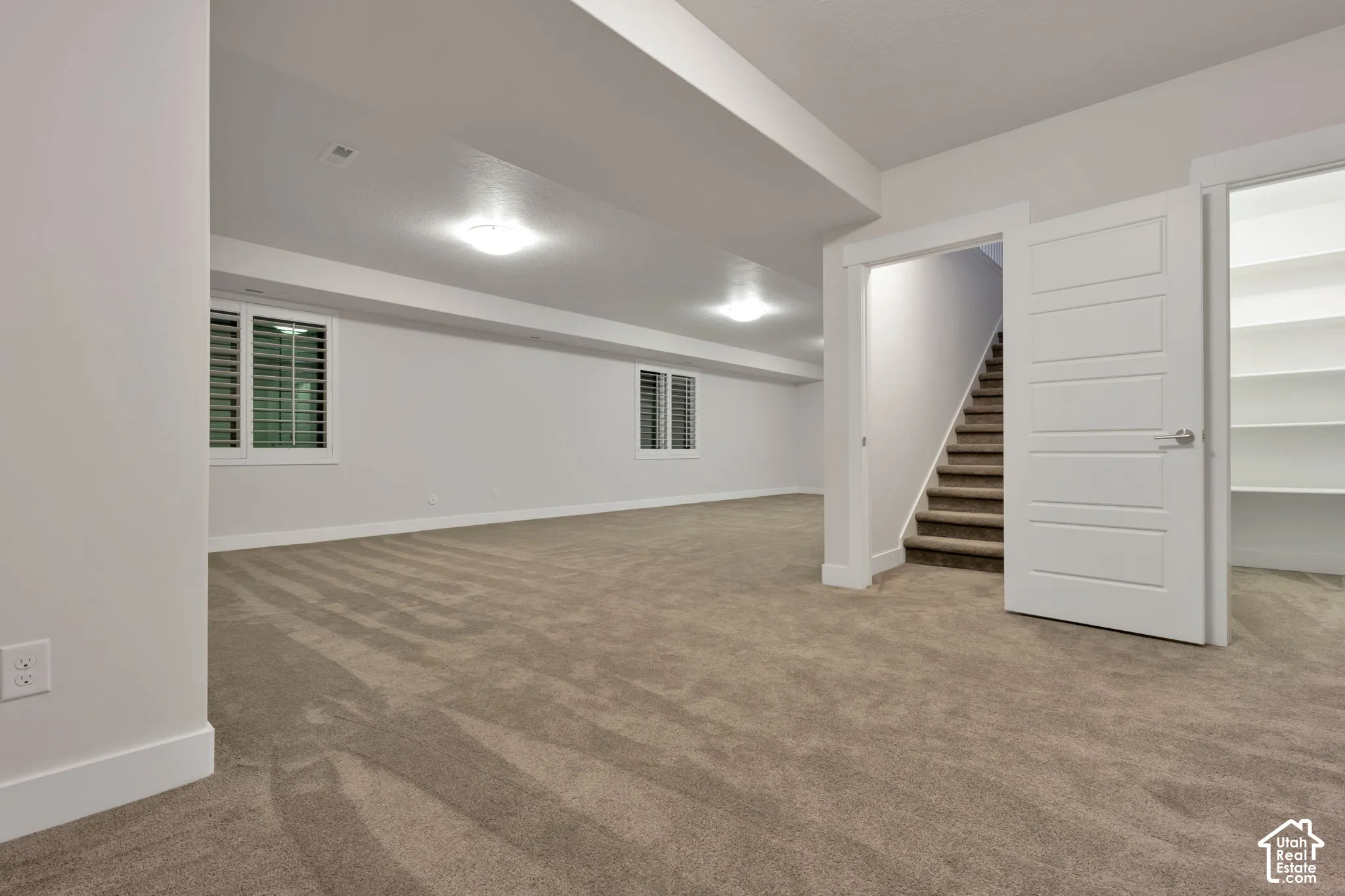 Open-concept room with neutral wall-to-wall carpeting, recessed flush-mount ceiling lighting, white interior doors, and built-in shelving