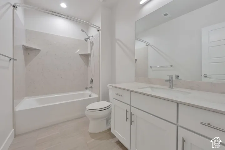 Bathroom featuring a white vanity with a light-toned solid surface countertop, an integrated sink, a large wall-mounted mirror, and a tub-shower combination with full-height surround panels
