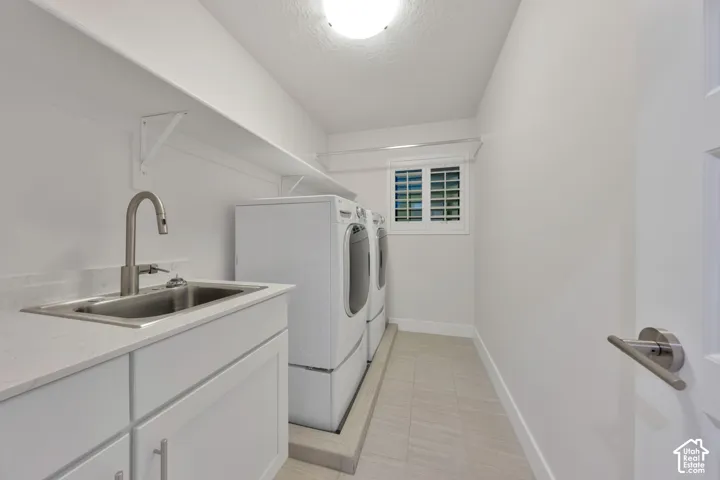 Laundry room featuring white cabinetry, a built-in stainless steel sink with a high-arc faucet, tile flooring, and plantation shutters