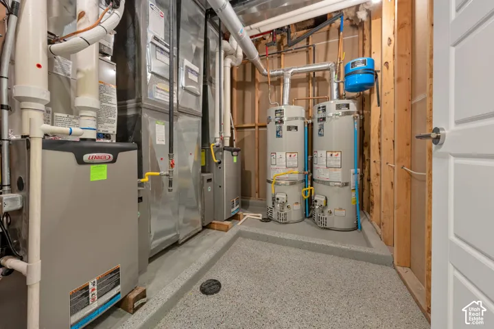 Utility room featuring dual water heaters, a forced-air furnace system, exposed structural framing, and a textured epoxy flooring surface