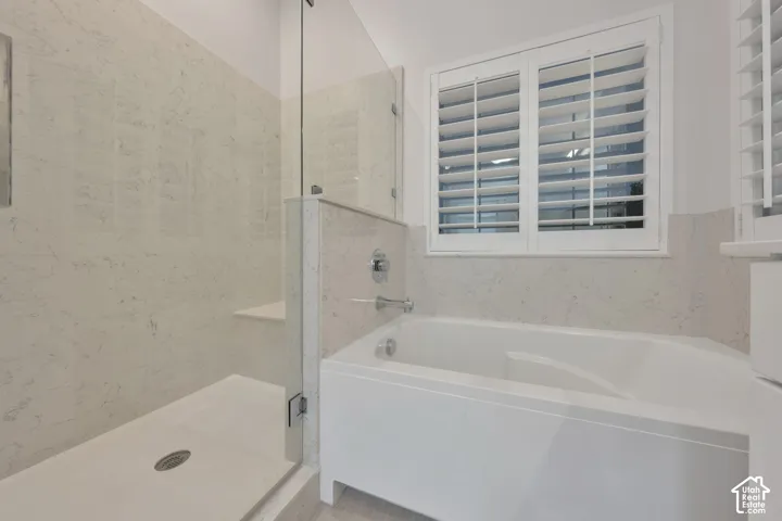 Walk-in shower with stone-surround wall tiling, built-in bench seat, and glass partition, alongside a deep soaking tub with chrome fixtures and plantation shutters