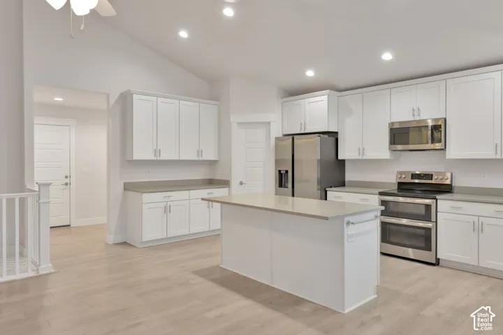 Kitchen featuring a vaulted ceiling, white shaker-style cabinetry, neutral-toned countertops, a center island, and wood-finish flooring