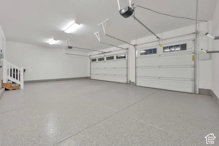 Three-car garage featuring epoxy-coated flooring, white paneled sectional doors with windows, bright overhead lighting, and white finished walls