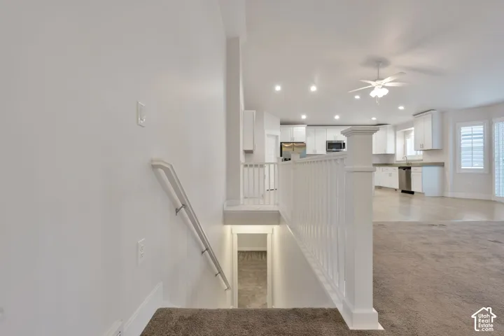 Staircase featuring white balusters and a wall-mounted handrail, recessed lighting, ceiling fan, and white kitchen cabinetry