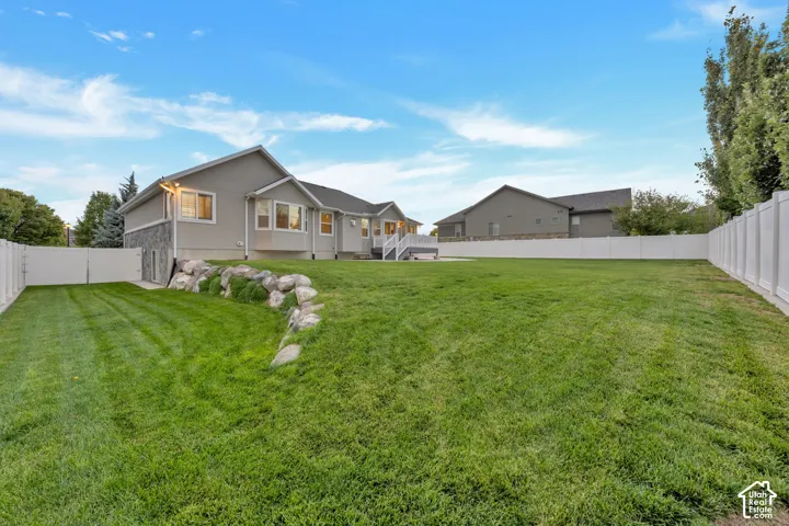 Expansive backyard featuring a tiered lawn, natural stone retaining wall, perimeter vinyl fencing, and an elevated composite deck