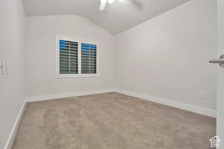 Room featuring a vaulted ceiling, neutral wall-to-wall carpeting, and a window with plantation-style shutters, complete with an attached ceiling fan