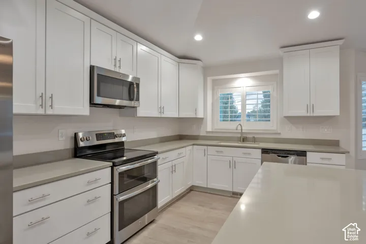 Kitchen featuring white shaker-style cabinetry, solid-surface countertops, stainless steel appliances, recessed ceiling lighting, and plantation shutters