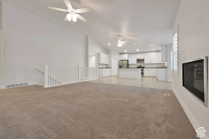 Open-concept floor plan featuring vaulted ceilings, recessed lighting, dual ceiling fans, a wall-mounted fireplace, and white cabinetry