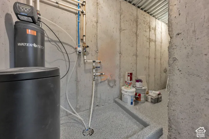 Utility area featuring poured concrete foundation walls, integrated water softener system, durable epoxy-coated flooring, and corrugated metal ceiling