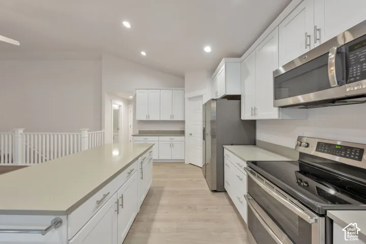 Kitchen featuring shaker-style cabinetry, solid-surface countertops, stainless steel appliances, and wood-finish flooring under a vaulted ceiling