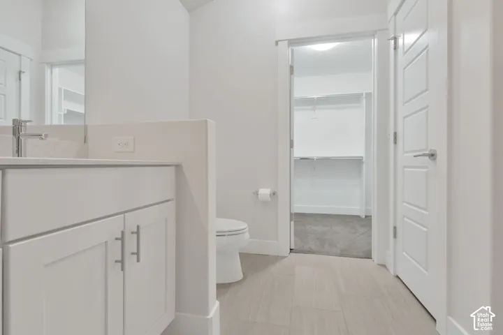 Bathroom featuring a vanity with shaker-style cabinetry, and rectangular undermount sink, complemented by light-toned tile flooring and a walk-in closet with built-in shelving