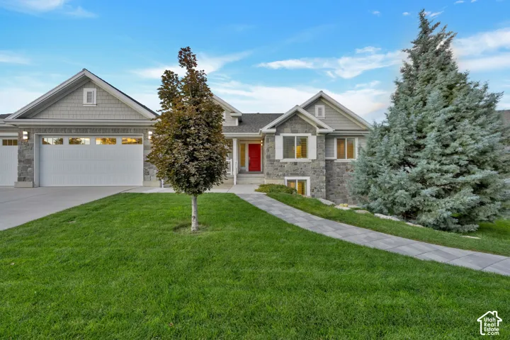 Stone veneer and shake siding exterior featuring a three-car garage, concrete driveway, paved walkway, and a vibrant red entry door