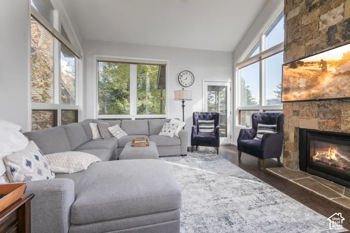 Vaulted ceiling with abundant natural light, stone-clad fireplace, and hardwood flooring