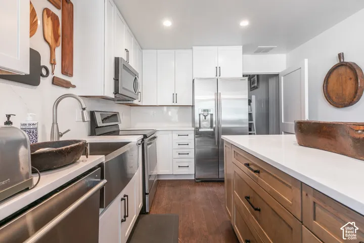 Modern kitchen with white cabinetry, stainless steel appliances, a farmhouse sink, light-toned countertops, and wood-finish flooring