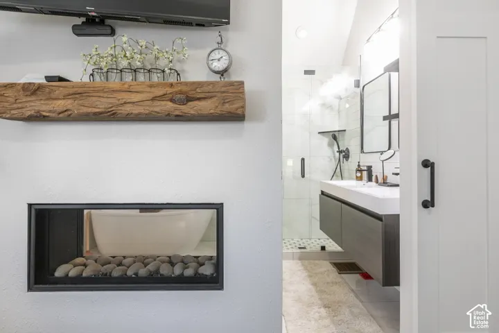 Recessed niche with decorative river stones, wood-finish floating shelf, and a contemporary bathroom featuring a floating vanity with integrated sink, glass-enclosed shower, and dark-toned fixtures