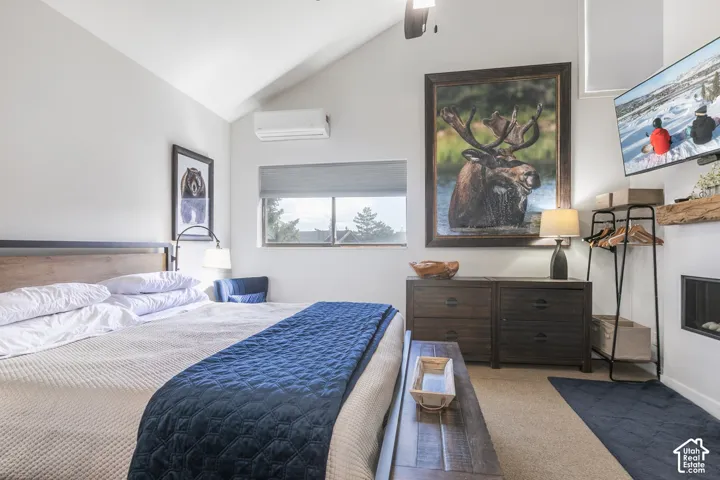 Vaulted ceiling, built-in fireplace, wood-finish headboard, window with roller shade, wall-mounted air conditioning unit