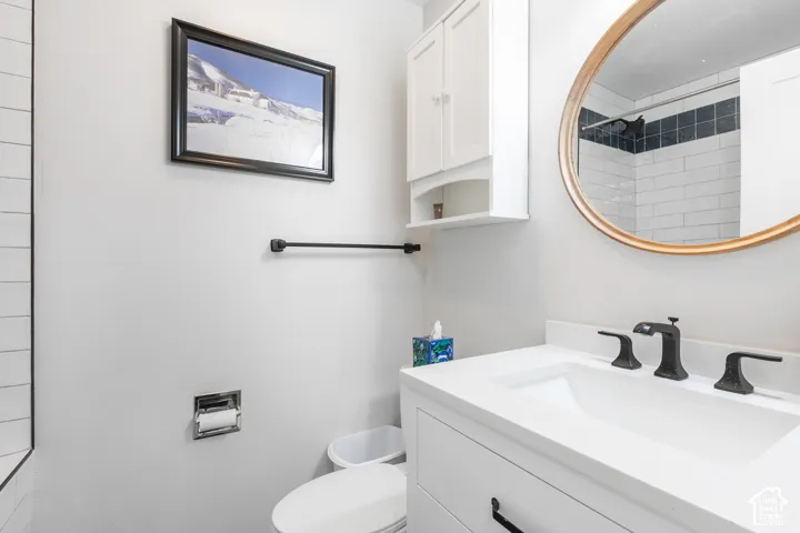 Modern bathroom featuring a white vanity with ample countertop space, matte black hardware and faucet, circular mirror with bronze-tone frame, subway tile surround, and white cabinetry with integrated storage
