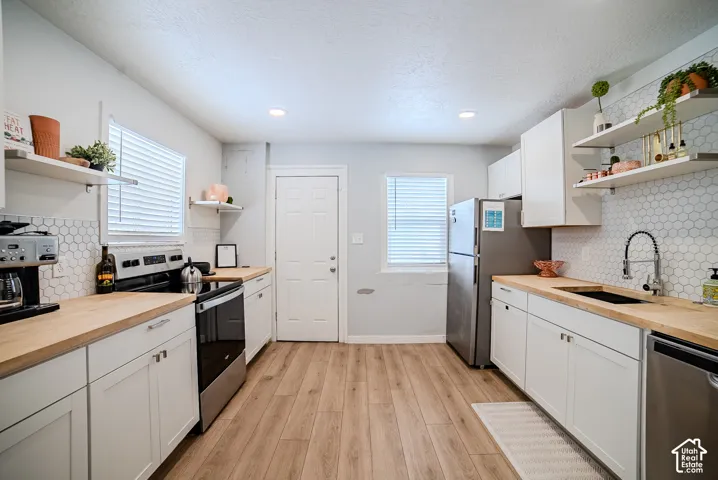 Kitchen featuring white shaker-style cabinetry, wood-finish countertops, hexagonal tile backsplash, stainless steel appliances, and wood-finish flooring