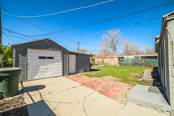 Detached garage with a single-car overhead door, brick patio, and fenced backyard