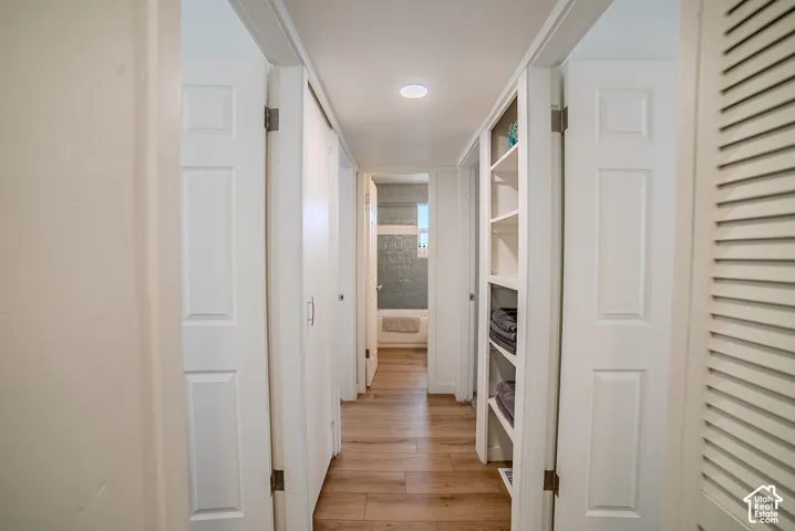 Hallway featuring wood-finish flooring, recessed lighting, built-in open shelving, and multiple six-panel doors