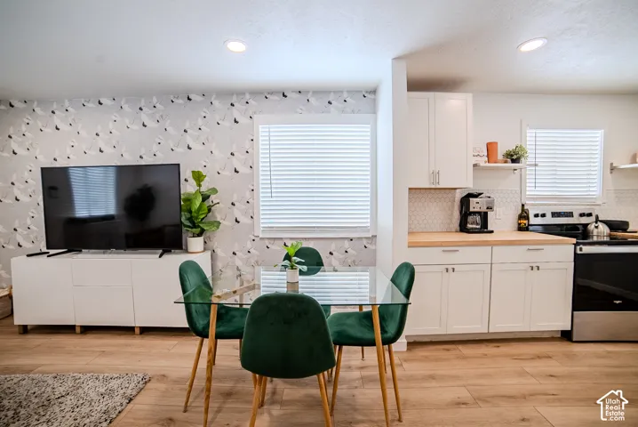 Wood-finish flooring, white shaker cabinetry, recessed ceiling lighting, hexagon tile backsplash, and patterned wall covering