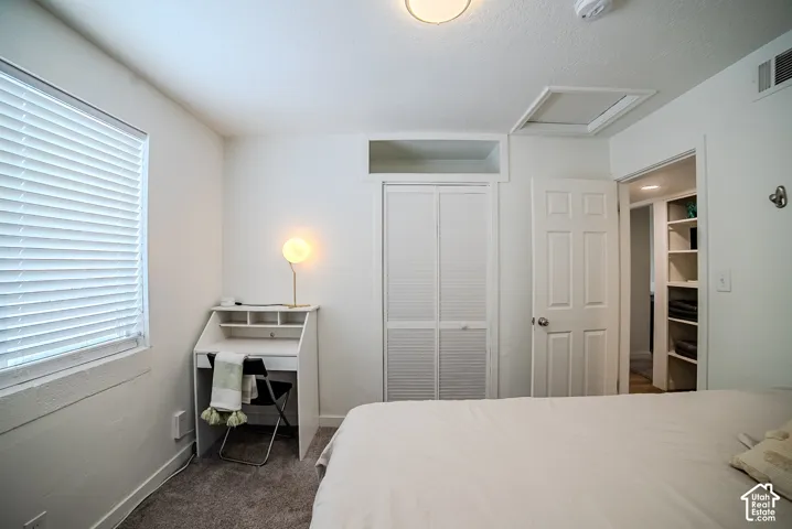 Neutral-toned room featuring louvered-panel closet doors, built-in recessed ceiling storage, six-panel interior door, and window with horizontal blinds