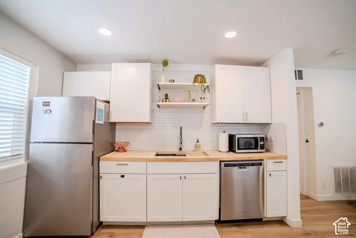 Kitchen featuring white shaker-style cabinetry, wood-finish countertops, stainless steel appliances, a hexagonal tile backsplash, and open shelving