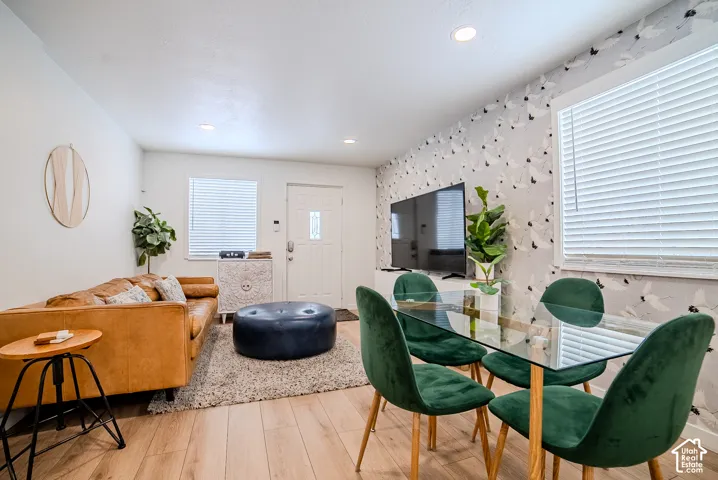 Wood-finish flooring, recessed lighting, and patterned wallpaper feature in this interior space, complete with multiple windows and a single entry door