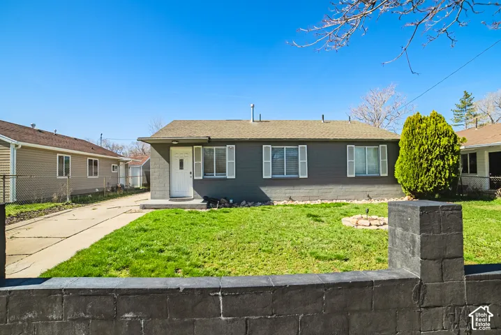 Single-story exterior featuring painted masonry siding, shutter-framed windows, a concrete driveway, and a decorative concrete block perimeter wall