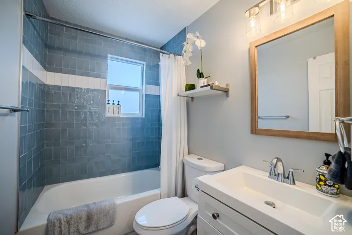 Bathroom featuring a deep-soaking tub, blue ceramic wall tile with white accent detailing, white vanity with an integrated rectangular sink, wood-finish framed wall mirror, and a three-light vanity fixture