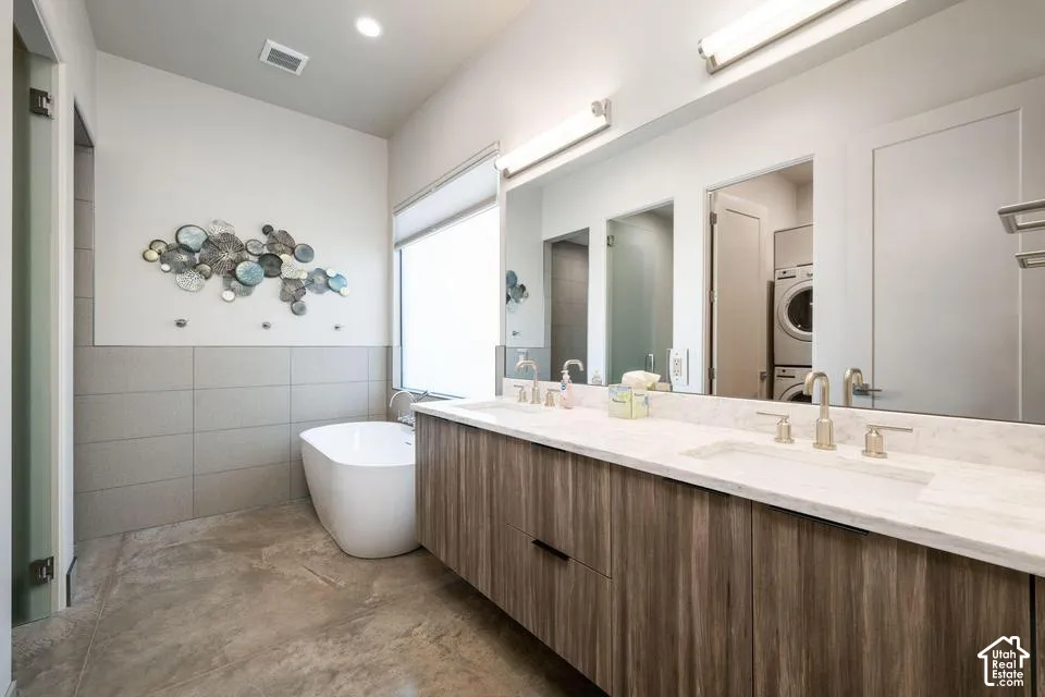 Floating wood-finish double vanity with stone countertop, dual undermount sinks, freestanding soaking tub, and floor-to-ceiling tile accents