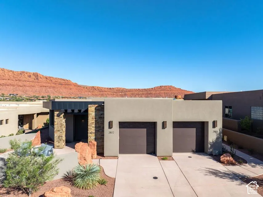 Contemporary exterior featuring smooth stucco finish, stone masonry accents, dual-car garage, and desert-inspired landscape design, set against a backdrop of red rock formations