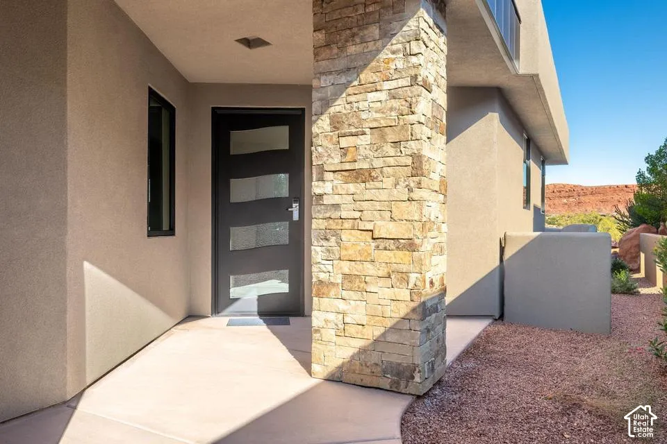 Entryway featuring a modern front door with horizontal glass panels, stacked stone column, and neutral stucco exterior finish