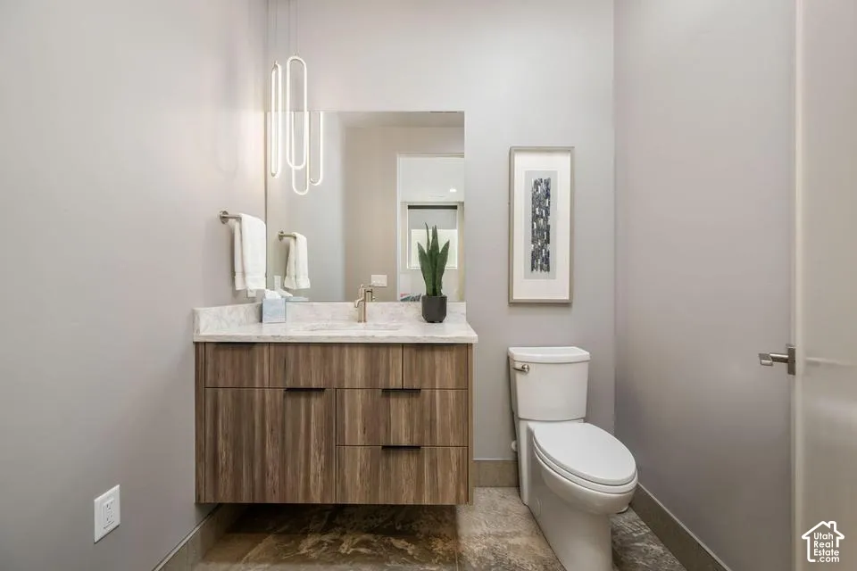 Floating wood-finish vanity with stone countertop, undermount sink, metallic faucet, modern vertical pendant lighting, and neutral stone-finish flooring