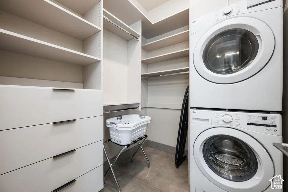 Dedicated laundry area featuring white custom cabinetry with flat-panel drawers, tiered open shelving, matte black hardware, and a stacked front-load washer and dryer set