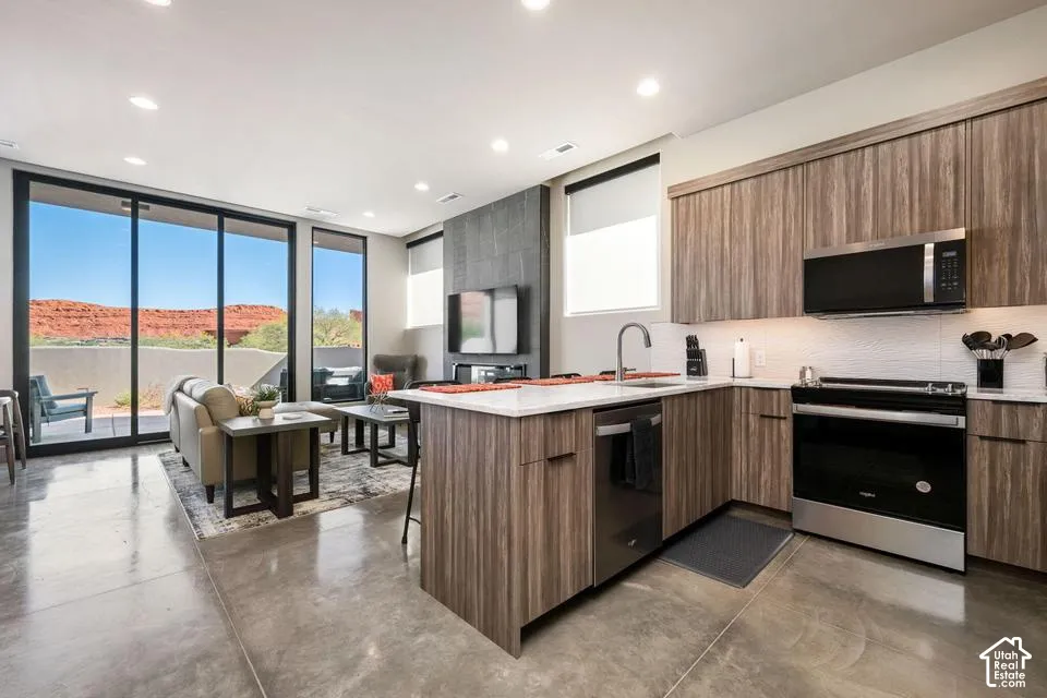 Kitchen featuring wood-finish cabinetry, stone-surface countertops, stainless steel appliances, polished concrete flooring, and full-height sliding glass doors