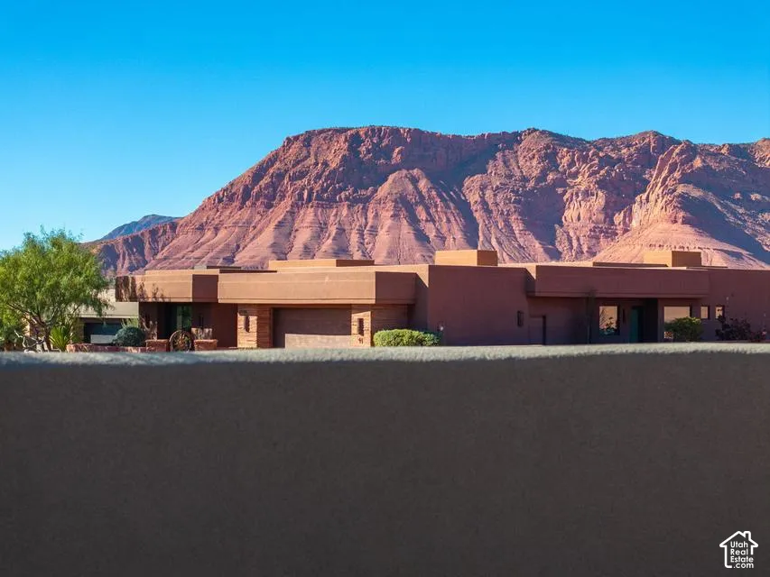 Single-story residence featuring a smooth stucco exterior, attached garage, stone accents, and red rock mountain scenery