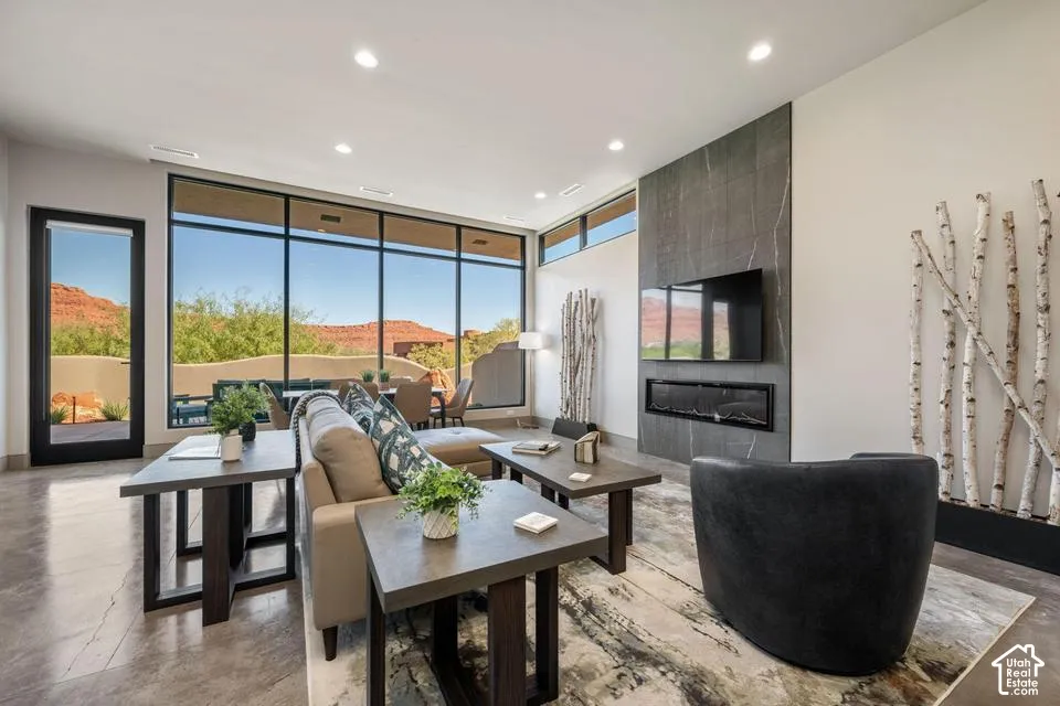 Living area featuring expansive floor-to-ceiling windows, polished concrete flooring, a floor-to-ceiling stone-tiled fireplace surround, and a linear built-in fireplace