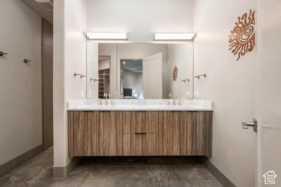 Floating dual-sink vanity featuring wood-finish cabinetry, stone countertop, integrated lighting, and wall-mounted faucets over large-format tile flooring
