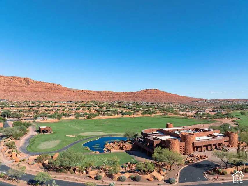 Aerial perspective of a multi-level structure with stone masonry exterior, circular towers, desert landscaping, water feature, and golf course surroundings against a mountainous backdrop