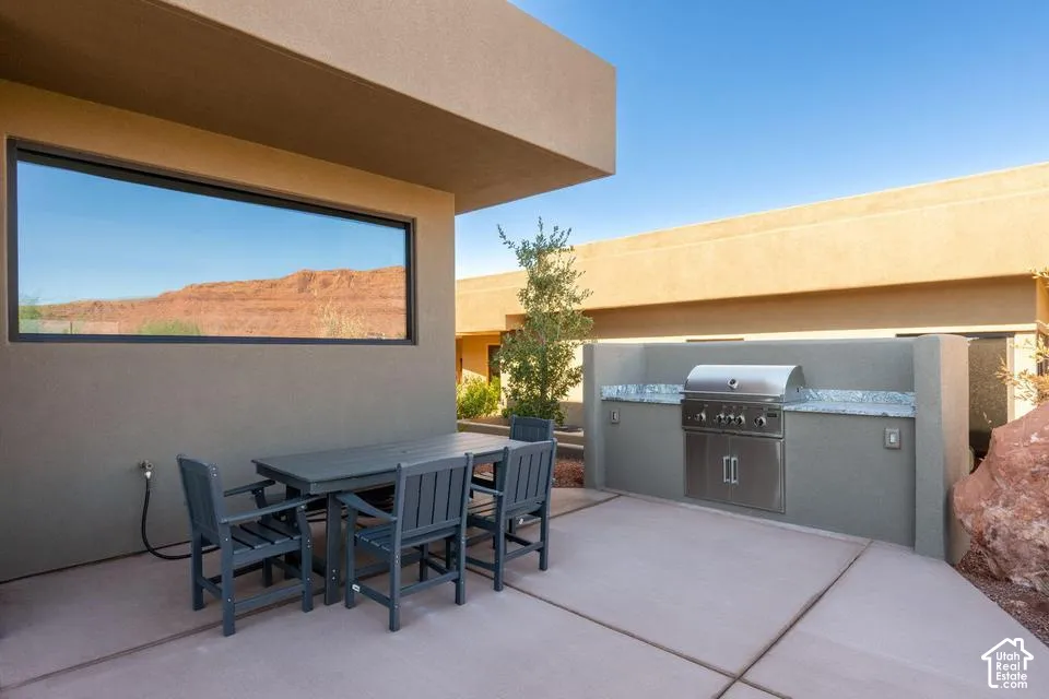 Covered patio featuring a built-in outdoor kitchen with stone countertop, stainless steel grill, concrete flooring, and red rock scenery