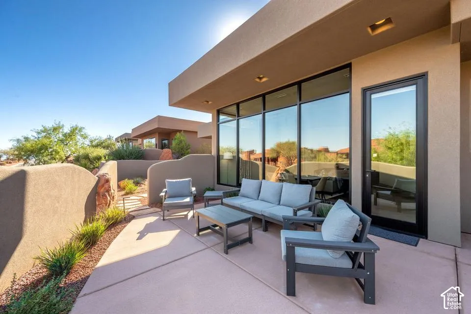 Concrete patio featuring a stucco privacy wall, floor-to-ceiling windows with black frames, and recessed lighting