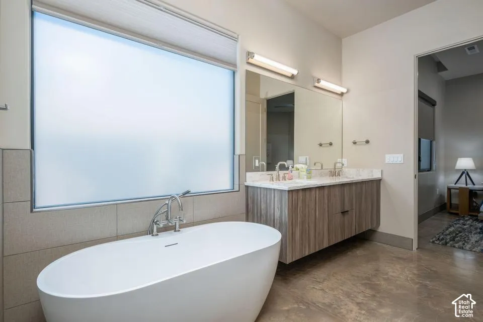 Freestanding soaking tub with a floor-mounted faucet, wall-mounted floating vanity featuring dual sinks and stone-finish countertops, and large-format wall tiling